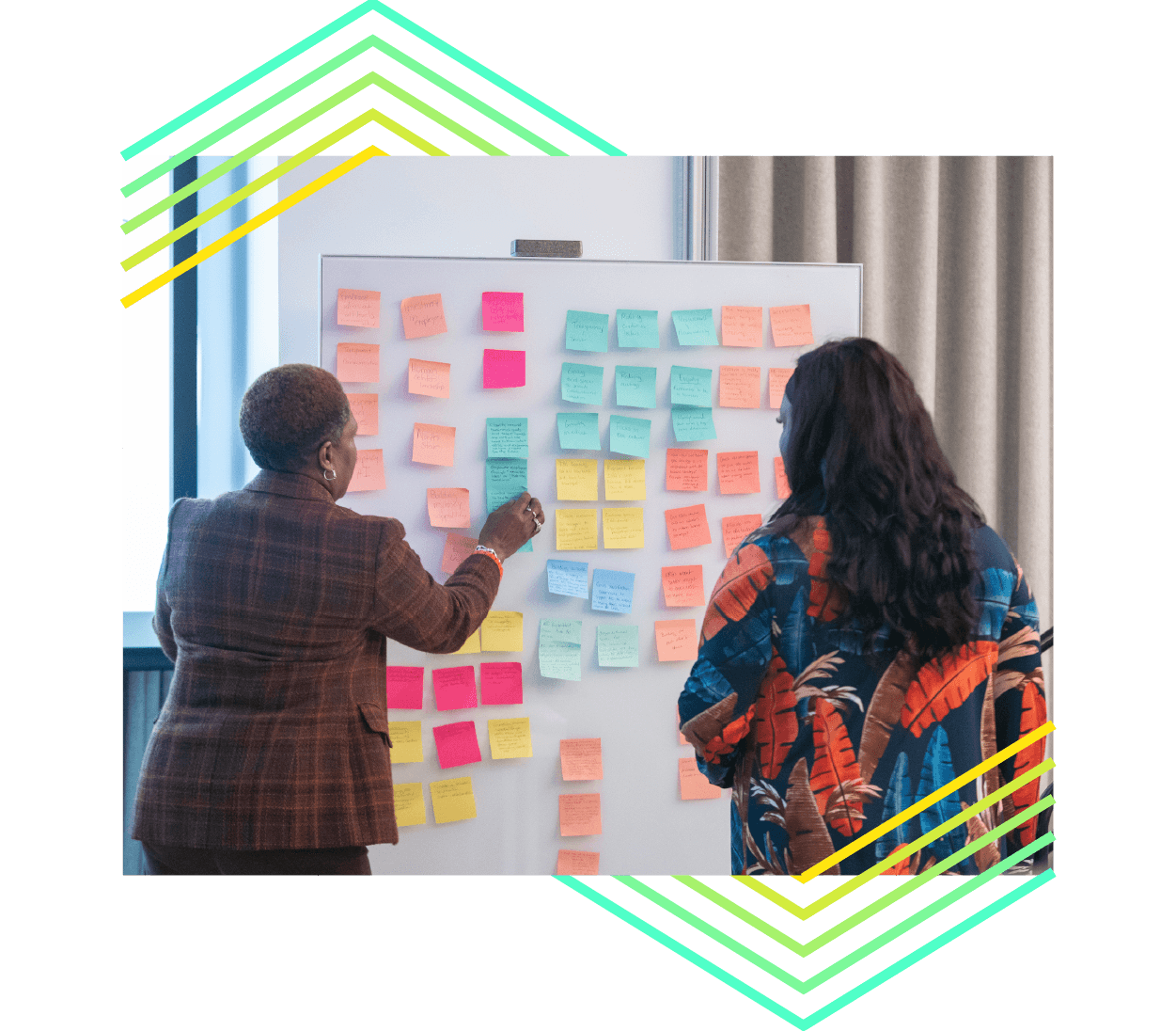 A photo of 2 people at a whiteboard with a variety of colored sticky notes in a working session.