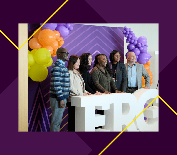 6 people standing in front of an ERG sign with a yellow, orange, and purple balloon arch behind them