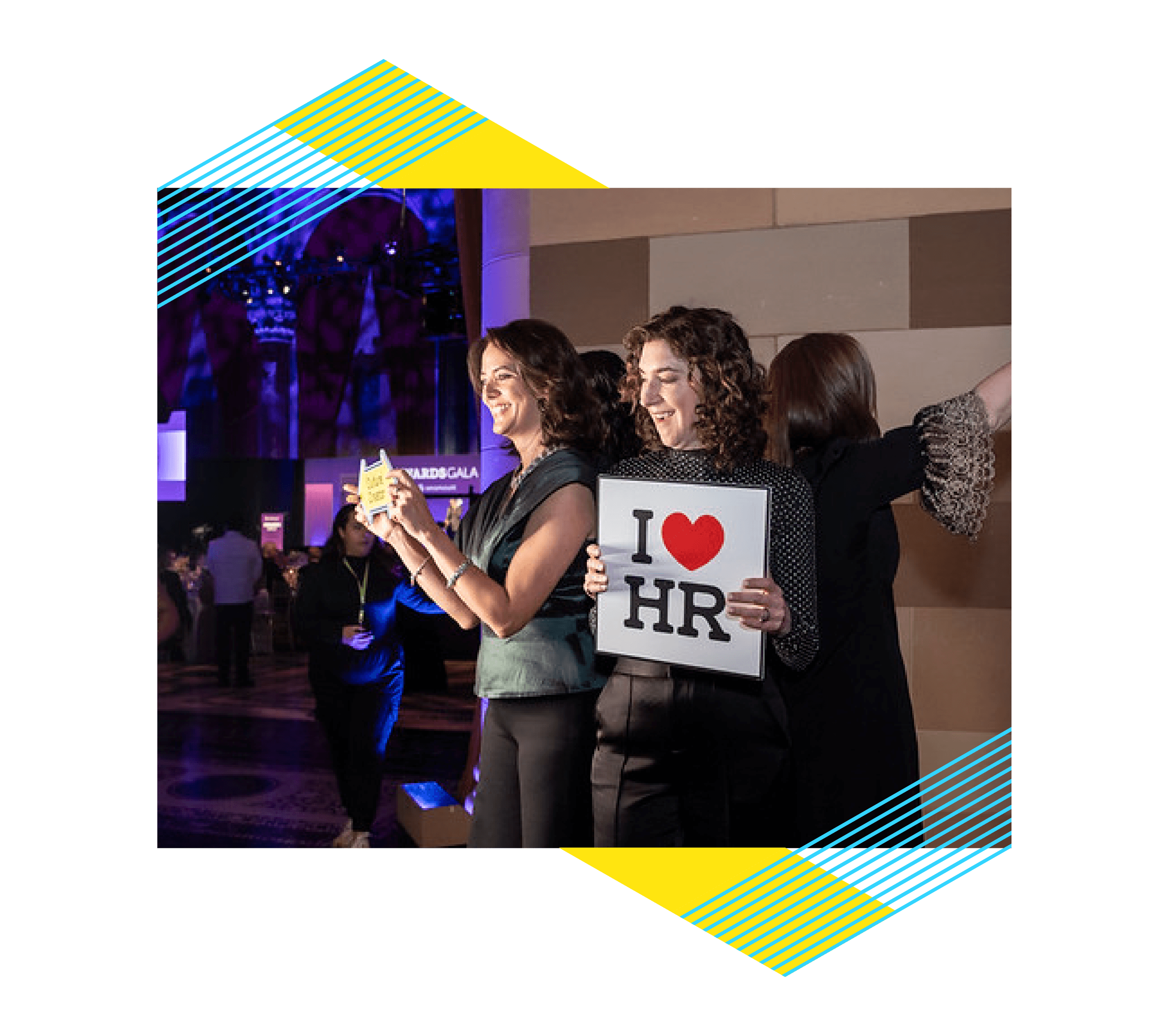 Two people at a photobooth, one person holding an "I heart HR" sign